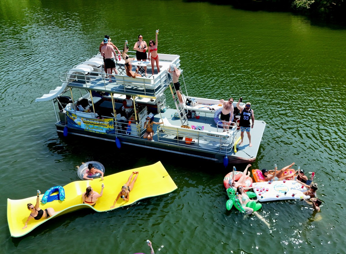 Groups of people enjoying a party on a boat and floating rafts on a lake.